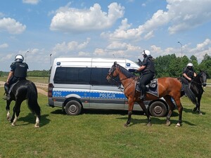 Policjanci na koniach krążą wokół radiowozu