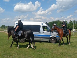 Policjanci jeżdżą na koniach wokół radiowozu