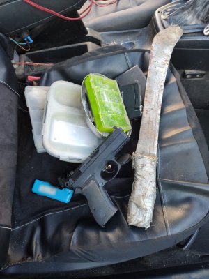 3 pudełka z zawartością białego proszku, kamera, maczeta, przedmiot przypominający broń, zapalniczka i waga elektroniczna na siedzeniu samochodu.