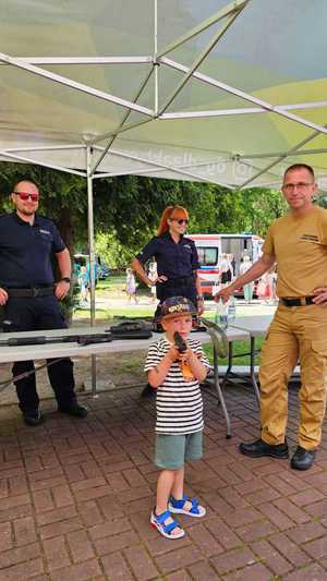 Na zdjęciu widzimy umundurowanych policjantów i strażaków oraz oznakowane radiowozy podczas pikniku mundurowego z okazji Dnia Dziecka.