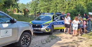 Na zdjęciu widzimy umundurowanych policjantów i strażników leśnych w trakcie działań na terenach zielonych. Mundurowi przeprowadzają rozmowy z wypoczywającymi na łonie natury.