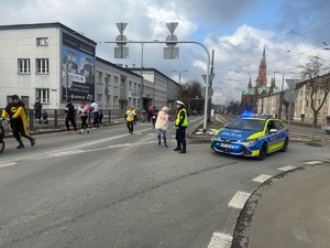 Umundurowani policjanci i radiowozy oznakowane, zabezpieczający bieg walentynkowy.