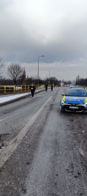 Umundurowani policjanci i radiowozy oznakowane, zabezpieczający bieg walentynkowy.