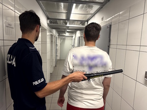 Zdjęcie przedstawia zatrzymanego z policjantem umundurowanym w pomieszczeniu dla osób zatrzymanych.