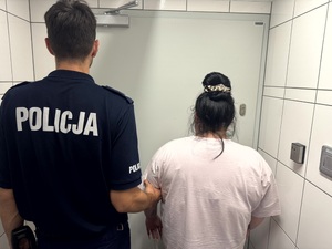 Zdjęcie przedstawia zatrzymaną z policjantem umundurowanym w pomieszczeniu dla osób zatrzymanych.