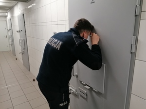 Umundurowany policjant patrzy przez wizjer do celi.