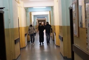 Dwóch policjantów na korytarzu konwojuje zatrzymanego młodego mężczyznę.