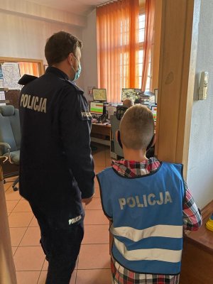 Po lewej policjant, po prawej chłopiec zaglądający do pomieszczenia dyżurnych.
