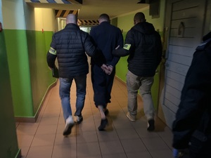 Na zdjęciu dwaj policjanci prowadzą podejrzanego korytarzem w podziemnym areszcie.