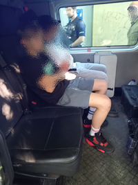 na zdjęciu dwóch nastolatków siedzących w policyjnym furgonie - pilnowani przez policjantów.