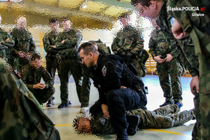 Na zdjęciu zamazana grupa żołnierzy a w środku wyraźny obraz policjanta - Sławomira Tokarza, który demonstruje chwyt judo.