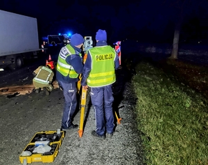 Na zdjęciu dwaj policjanci mierzą specjalnym urządzeniem miejsce wypadku drogowego.