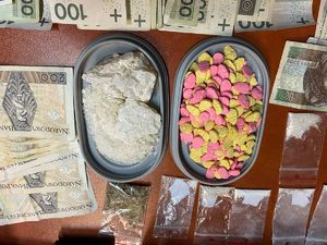 Na zdjęciu dwa pudełka z narkotykami w postaci kryształu po lewej i tabletek po prawej. Wszystko to otoczone banknotami.