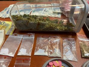 Na zdjęciu słój z substancją susz marihuany. Wokół torebki strunowe, widać tez banknoty.