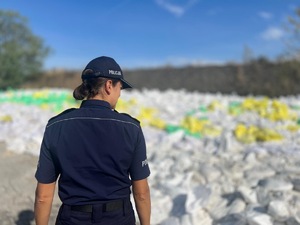 Na zdjęciu policjanta spoglądająca na worki przy wale powodziowym