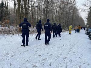 na zdjęciu kolumna poszukiwaczy - funkcjonariuszy policji i straży idąca droga leśną