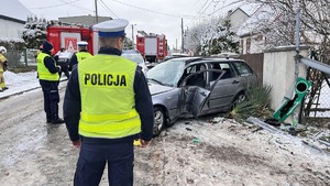 Na zdjęciu widzimy policjantów dokonujących oględziny samochodu, który uderzył bokiem w ogrodzenie.