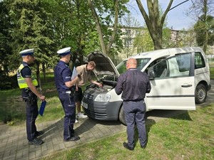 test obsługi technicznej pojazdu - uczeń egzaminator i dwóch umundurowanych policjantów stoją przy otwartej masce samochodu i sprawdza olej
