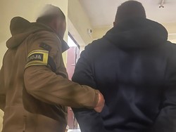 Policjant nieumundurowany ( z opaską na ręce POLICJA), prowadzi zatrzymanego.