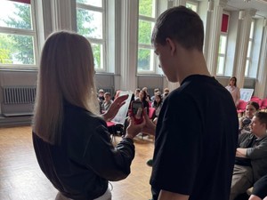 Tyłem stoi kobieta w długich blond włosach wraz z uczniem, który prowadzi badanie na zawartość dwutlenku węgla w organizmie.