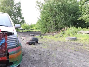 Fragment stojącego samochodu oraz leżące opony na ziemi. W tle widać drzewa