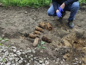 Na ziemi leży kilka niewybuchów, obok widać klęczącego mężczyznę.
