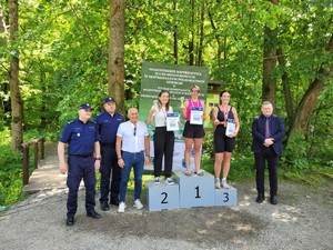 Trzy policjantki stojące na zwycięskim podium. Obok dwóch umundurowanych policjantów i jeden mężczyzna w garniturze.
