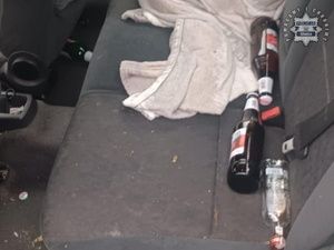 Zdjęcie przedstawia butelki po alkoholu leżące na tylnej kanapie pojazdu.