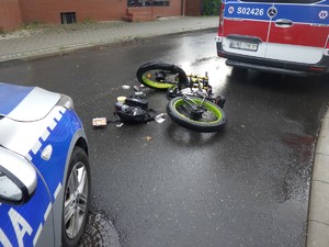 Na jedni pomiędzy karetką pogotowia a pojazdem Policji leży motorower.