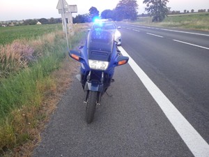 Na poboczu stoi oznakowany radiowóz Policji. Przed nim motocykl granatowy.