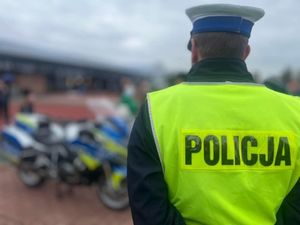 Policjant w kamizelce odblaskowej, stojący tyłem.