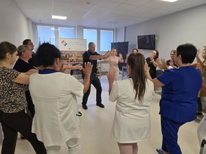 Praktyczna nauka samoobrony. Pracownicy wykonują ćwiczenia stojąc o okręgu wraz z umundurowanym policjantem.