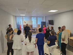 Praktyczna nauka samoobrony. Pracownicy wykonują ćwiczenia stojąc o okręgu wraz z umundurowanym policjantem.