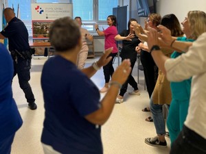 Praktyczna nauka samoobrony. Pracownicy wykonują ćwiczenia stojąc o okręgu wraz z umundurowanym policjantem.