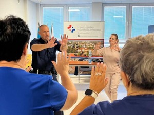 Praktyczna nauka samoobrony. Pracownicy wykonują ćwiczenia stojąc o okręgu wraz z umundurowanym policjantem.