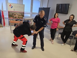Umundurowany policjant pokazuje chwyty obezwładniające na ratowniku.