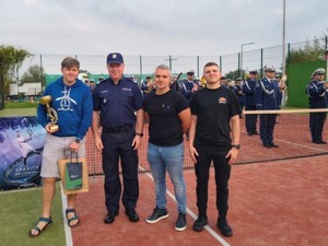 Na zdjęciu na boisku stoi Zastępca Komendanta Głównego Policji wraz z trzema nieumundurowanymi policjantami. W tle stoi orkiestra policyjna.