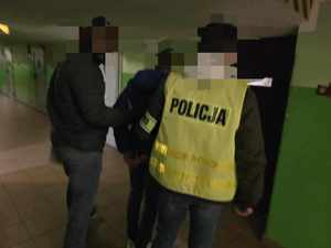 Policjanci stoją przy drzwiach wyjściowych z zatrzymanym