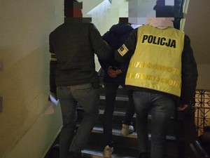 Policjanci prowadzą po schodach zatrzymanego.