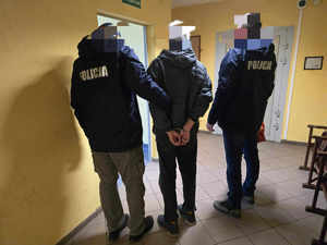 Dwóch policjantów prowadzi zatrzymanego korytarzem.