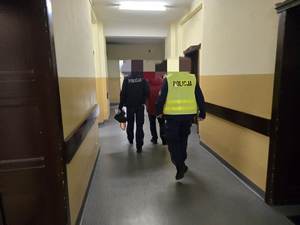 Dwóch policjantów umundurowanych prowadzi zatrzymanego korytarzem.