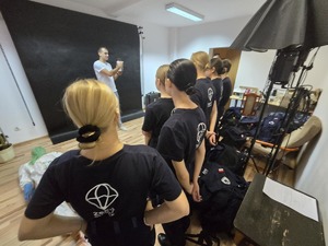 Zajęcia dla uczniów klasy policyjnej prowadzi technik kryminalistyki. Dookoła niego w pokoju stoją uczniowie.