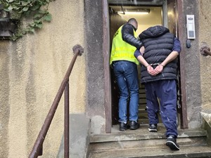 Policjant wprowadza zatrzymanego w kajdankach do komendy.