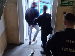 Policjanci wyprowadzają z budynku zatrzymanego mężczyznę.
