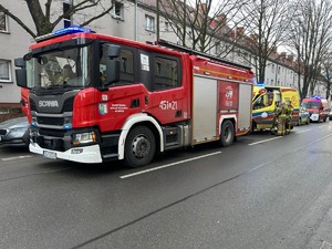 Na zdjęciu na ulicy stoi straż pożarna oraz karetka pogotowia i radiowóz Policji. Strażacy stoją koło pojazdu.
