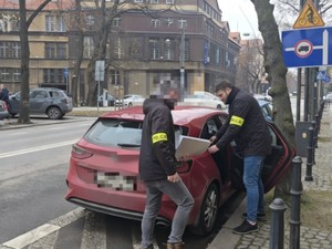 Na zdjęciu przy samochodzie nieoznakowanym dwóch policjantów bez umundurowania prowadzi zatrzymanego.