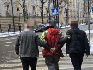 Dwóch nieumundurowanych policjantów prowadzi zatrzymanego mężczyznę.