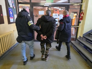 Zatrzymany i policjanci wychodzą przez przeszklone drzwi.