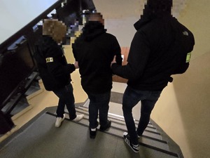 Policjanci po schodach prowadzą do wyjścia zatrzymanego