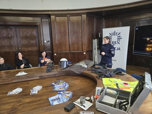 Policjantka prowadzi dla uczniów pogadankę. Uczniowie siedzą przy stole.